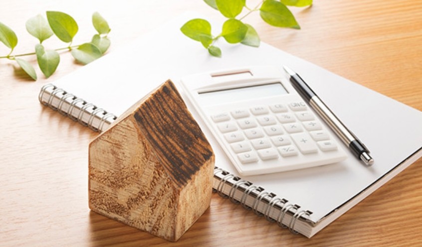 積み木の家の隣にノート、電卓、ペンが置いてある写真